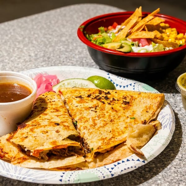 Quesadillas, a side of broth, salsa, and a salad with tortilla strips on a speckled table.